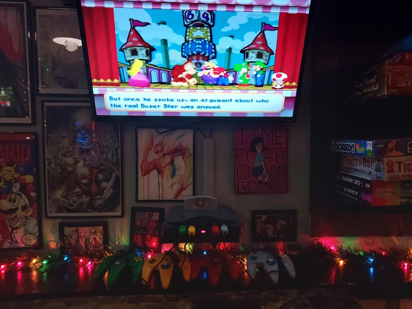 Inside Club Geek: a screen running a game, framed art on the walls and string lights along the shelf.