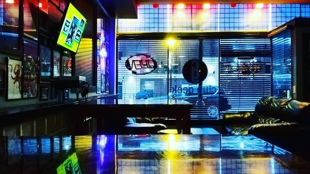 The front window of Club Geek at night, seen from inside, with a neon open sign.